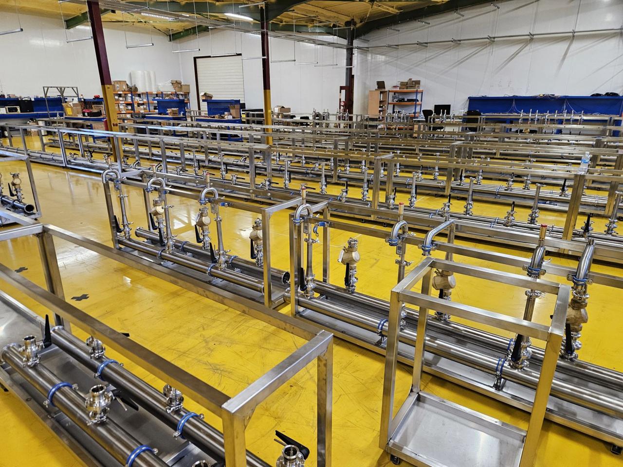 Production floor with multiple long stainless steel cooling manifold assemblies on yellow factory deck